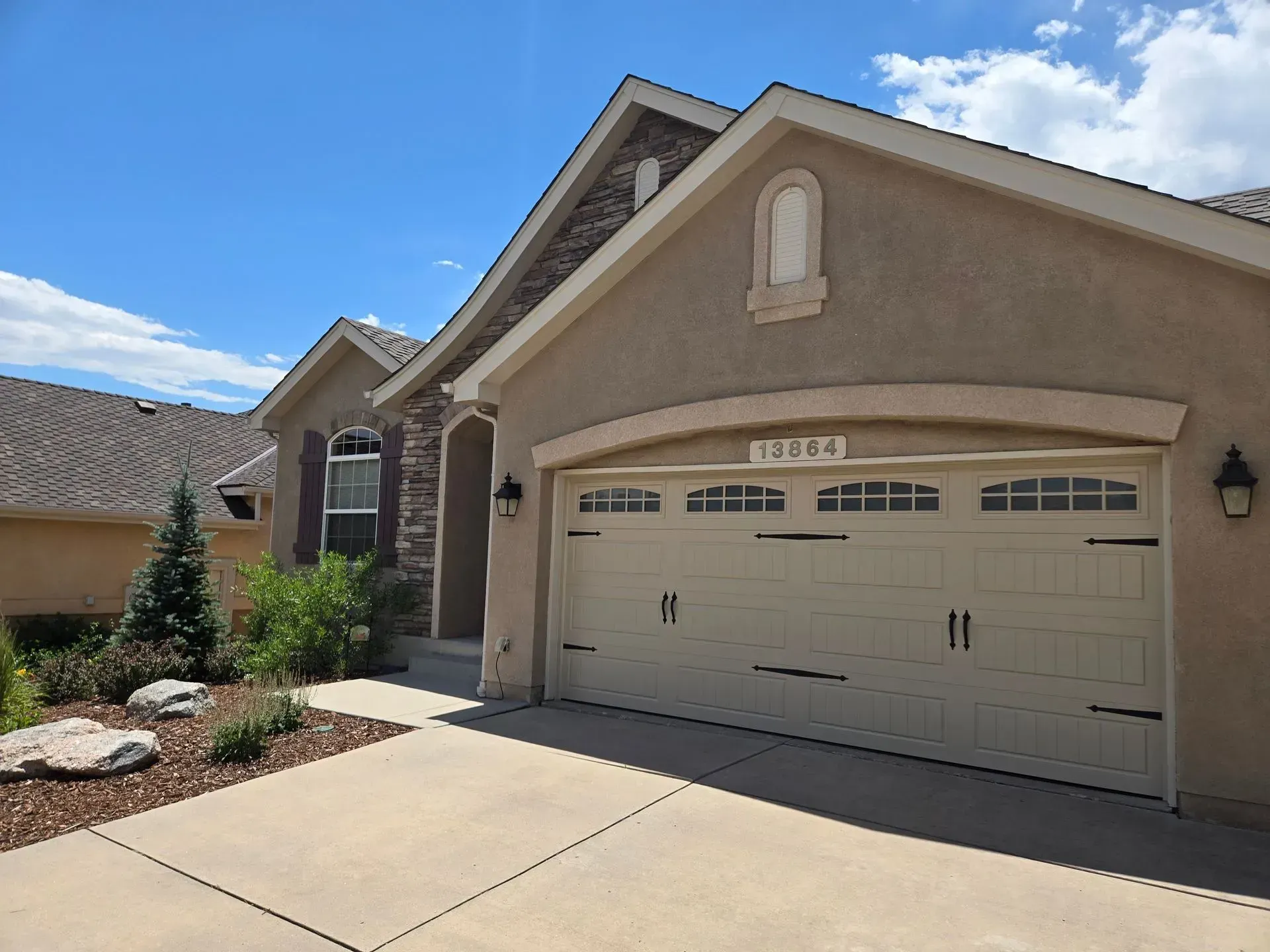 Beige house with a two-car garage, stone accents, and a blue sky.