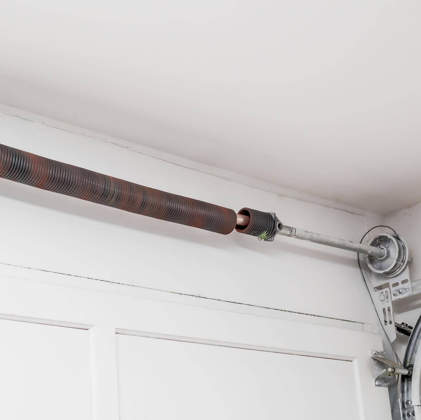 Garage door spring mechanism with a rusty spring and pulley system.