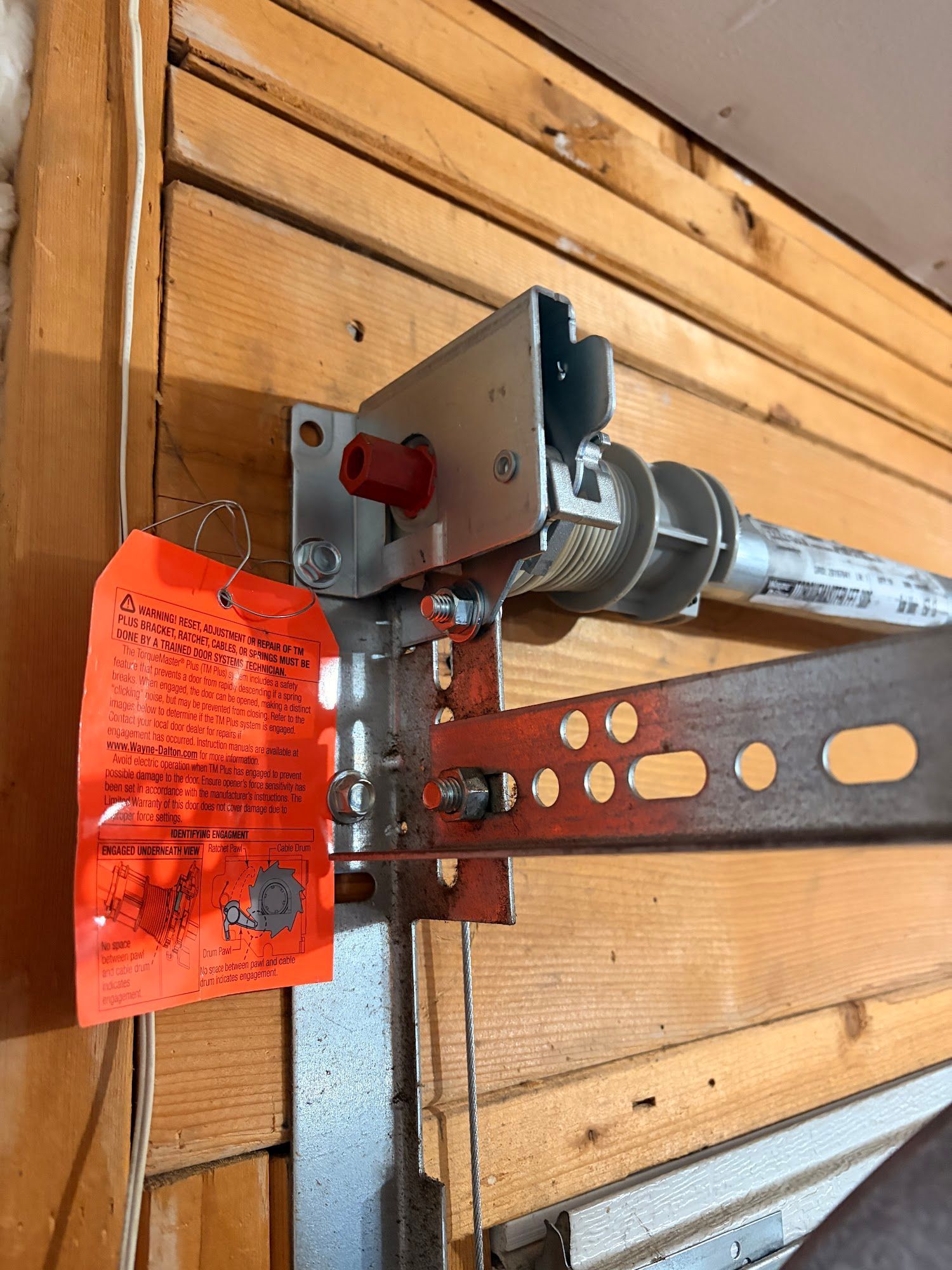 Garage door opener mechanism mounted on wooden wall; orange tag attached.