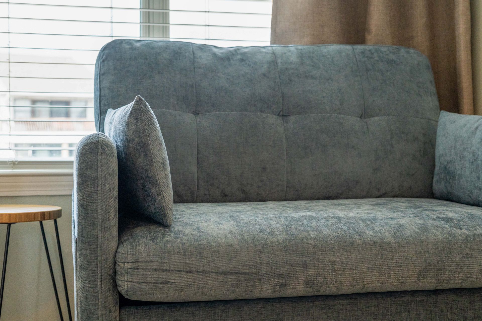 A grey couch is sitting in front of a window in a living room.