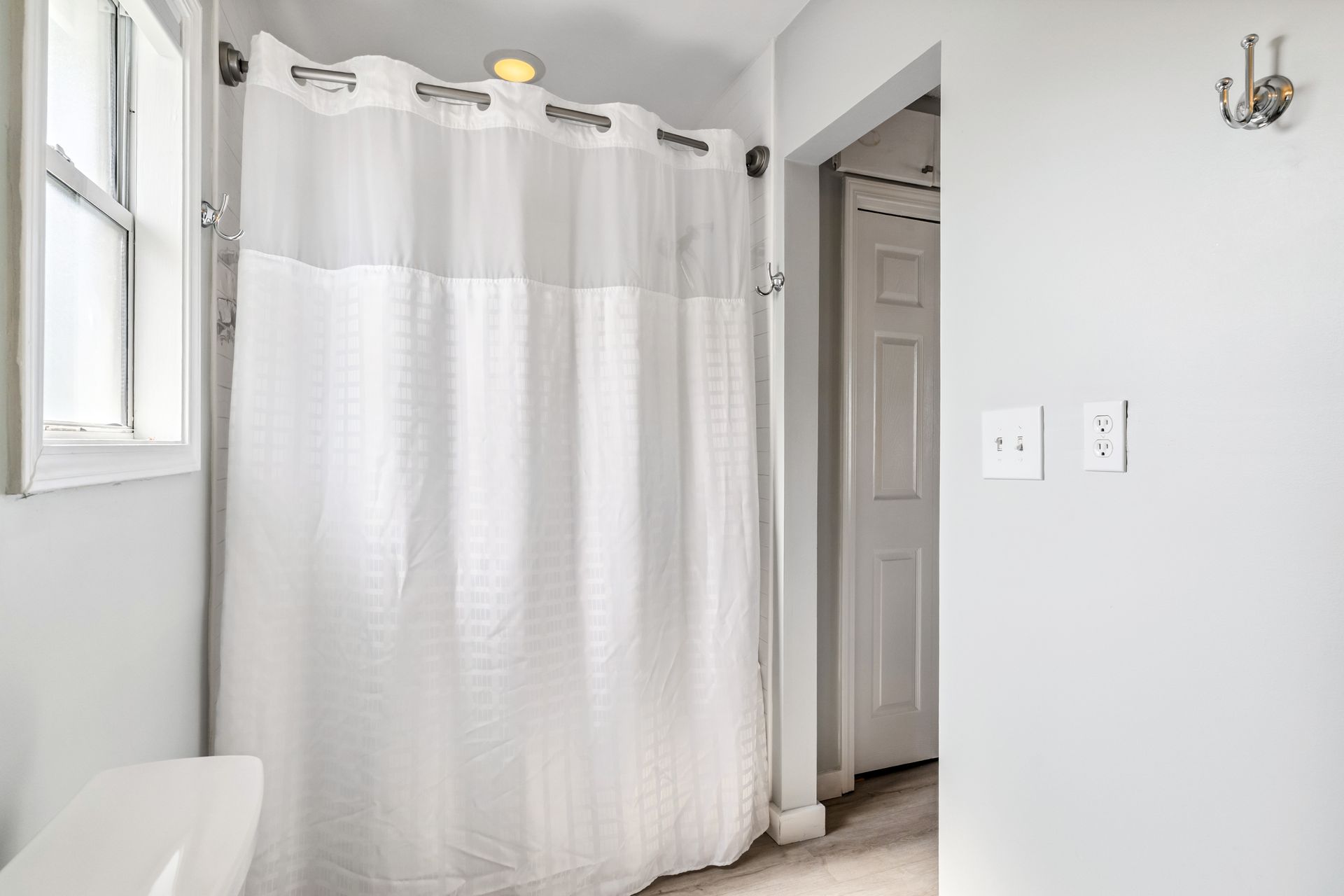 A bathroom with a white shower curtain and a window.