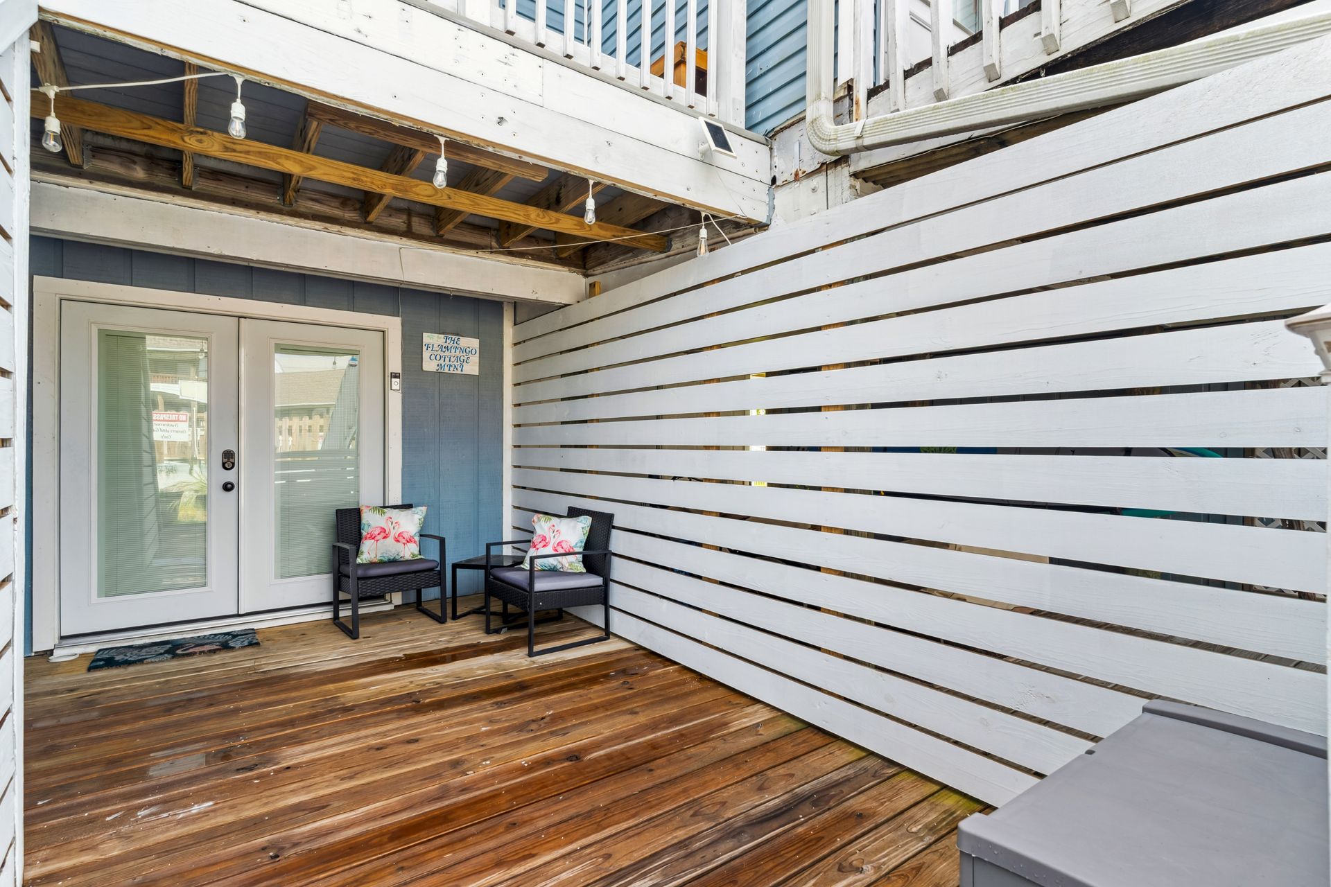 A wooden deck with chairs and a table in front of a white fence.