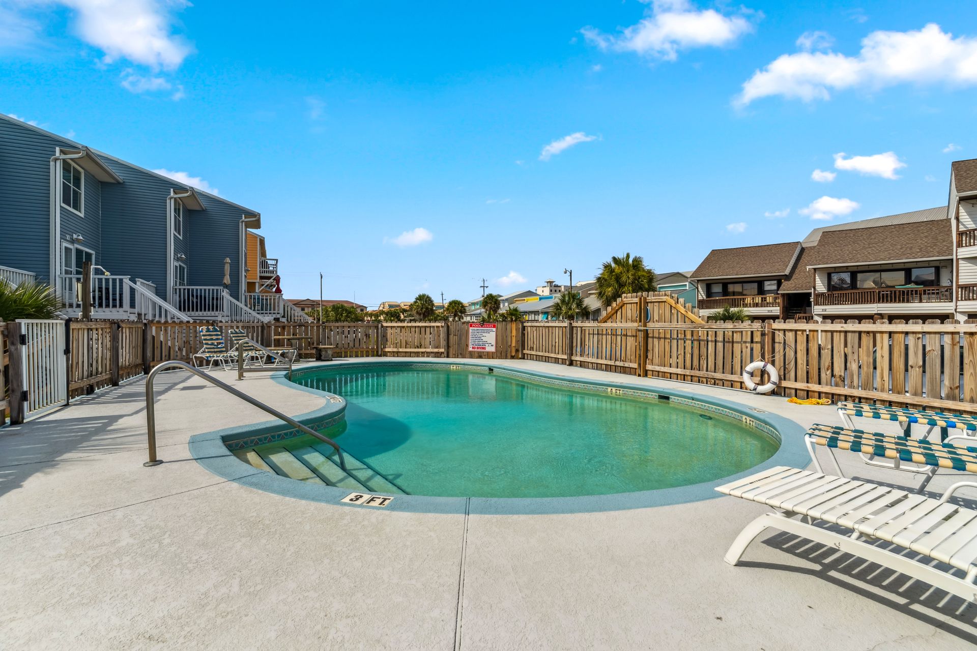 A large swimming pool is surrounded by a fence and chairs.