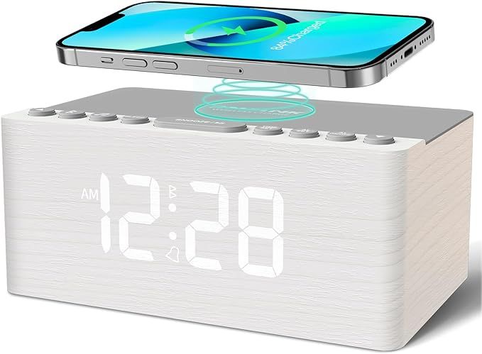 A white clock with a cell phone sitting on top of it.