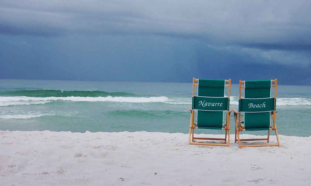 Two green beach chairs on a beach with a stormy sky in the background