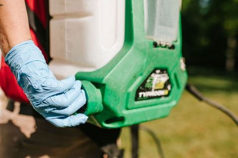 Gloved hand holding a green power tool against an outdoor grassy background