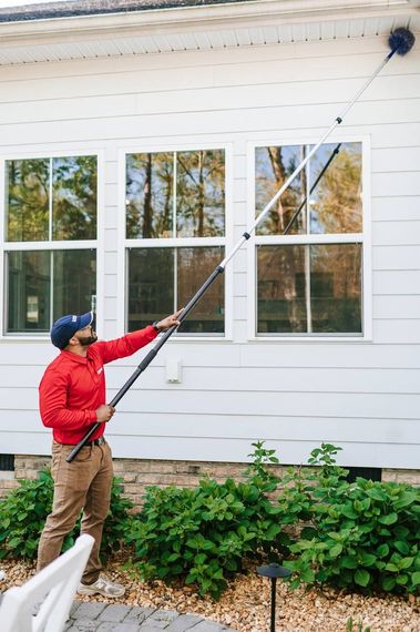 Worker in red uniform spraying pesticide along a house foundation with a backpack sprayer