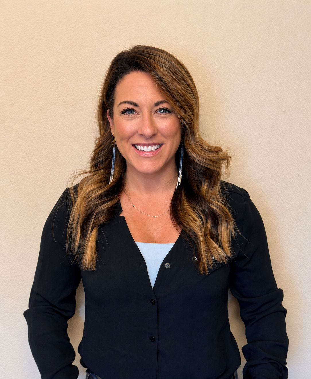 Smiling woman in a black blouse standing against a beige wall