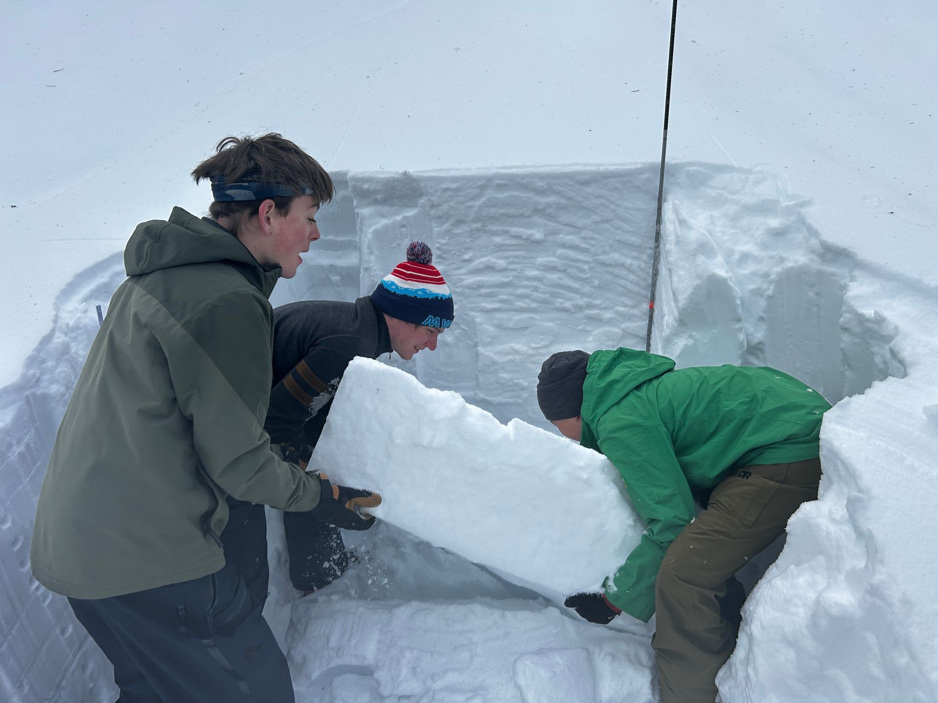 Children posing with skis on a snowy slope, wearing colorful winter gear and helmets.