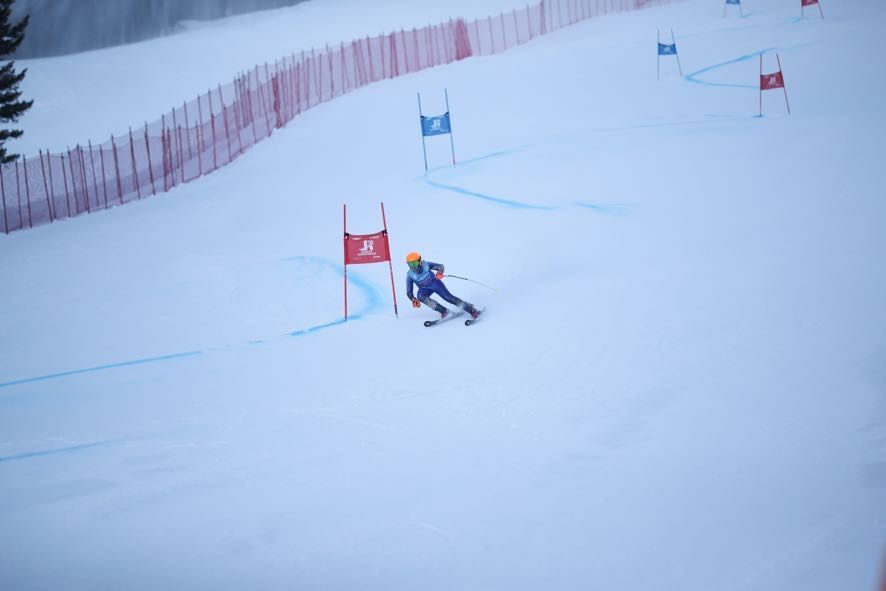Skier carving past a red gate on a snowy slalom course with other gates ahead