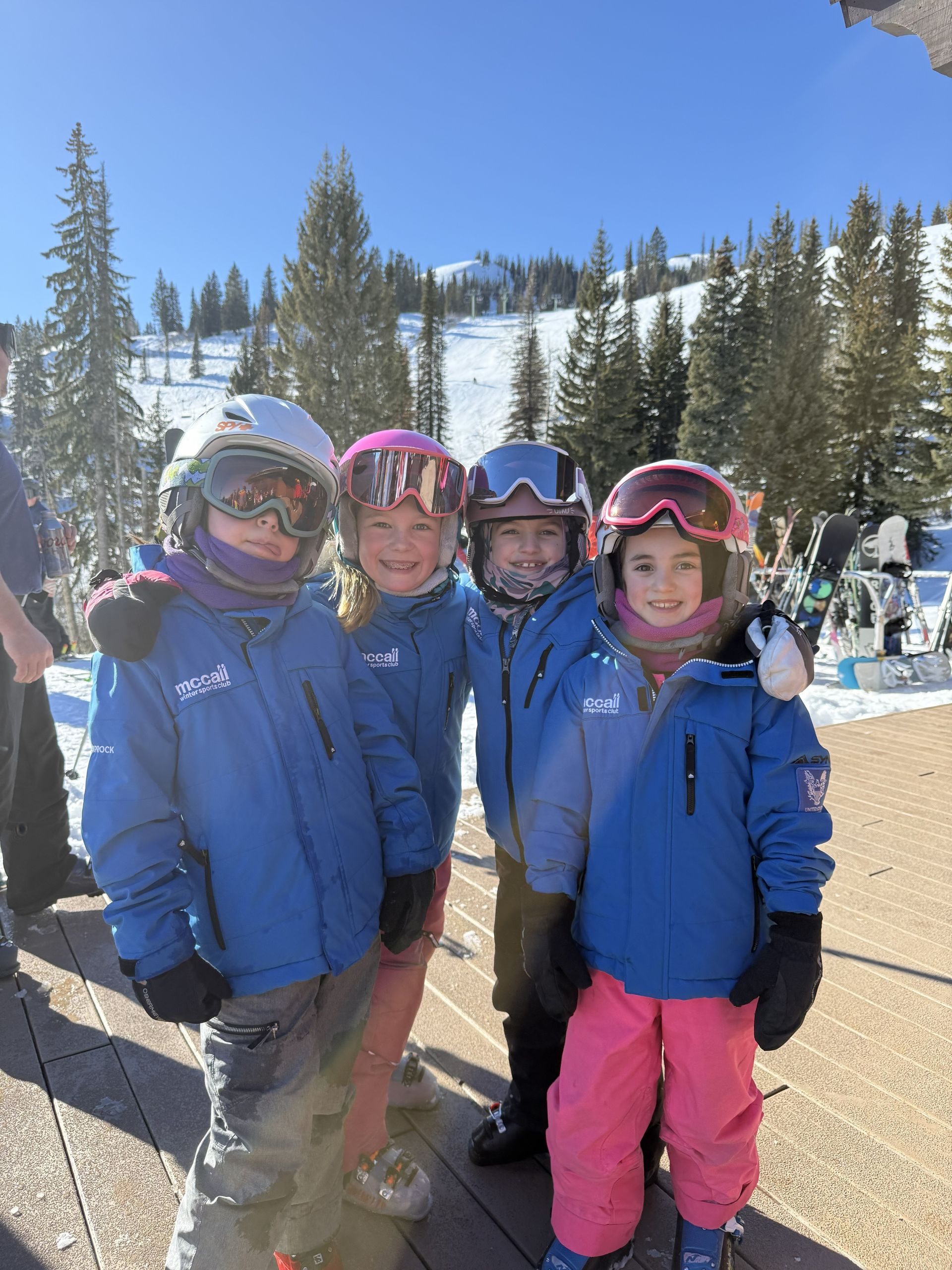 Four skiers in blue jackets posing on a snowy mountain slope under a clear sky