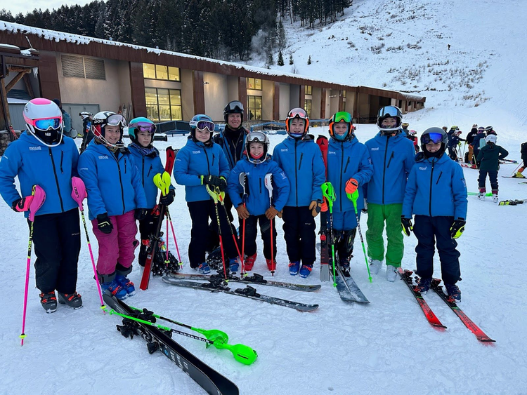 Group of skiers in blue jackets posing on a snowy slope with skis and poles, lodge in background