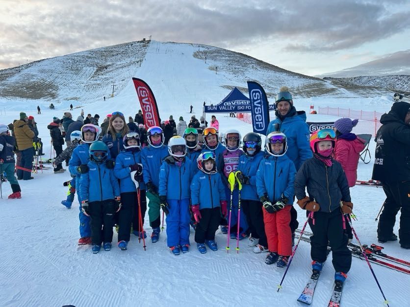Group of skiers in blue jackets posing on a snowy slope with mountains in the background