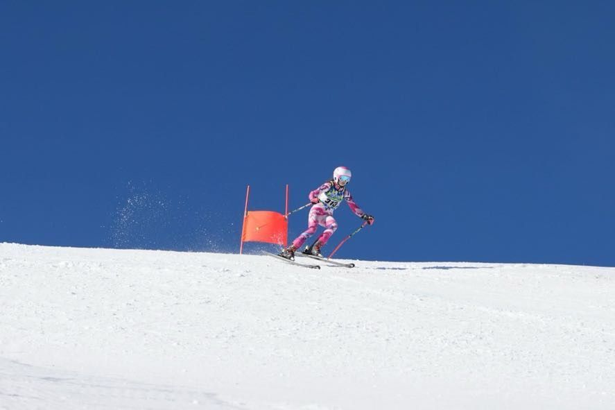 Skier in pink racing downhill past an orange gate on a snowy slope under a blue sky