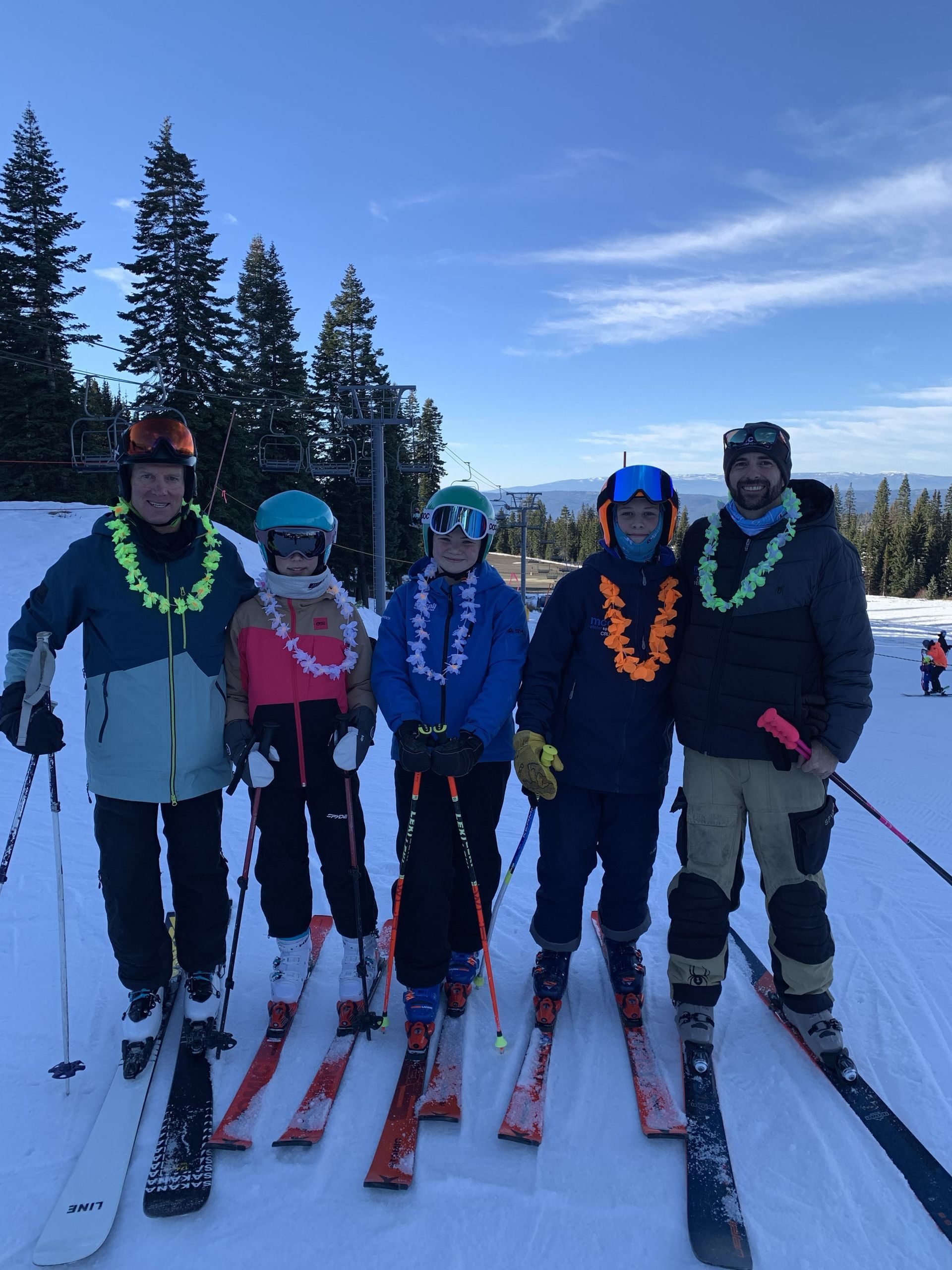 Children posing with skis on a snowy slope, wearing colorful winter gear and helmets.