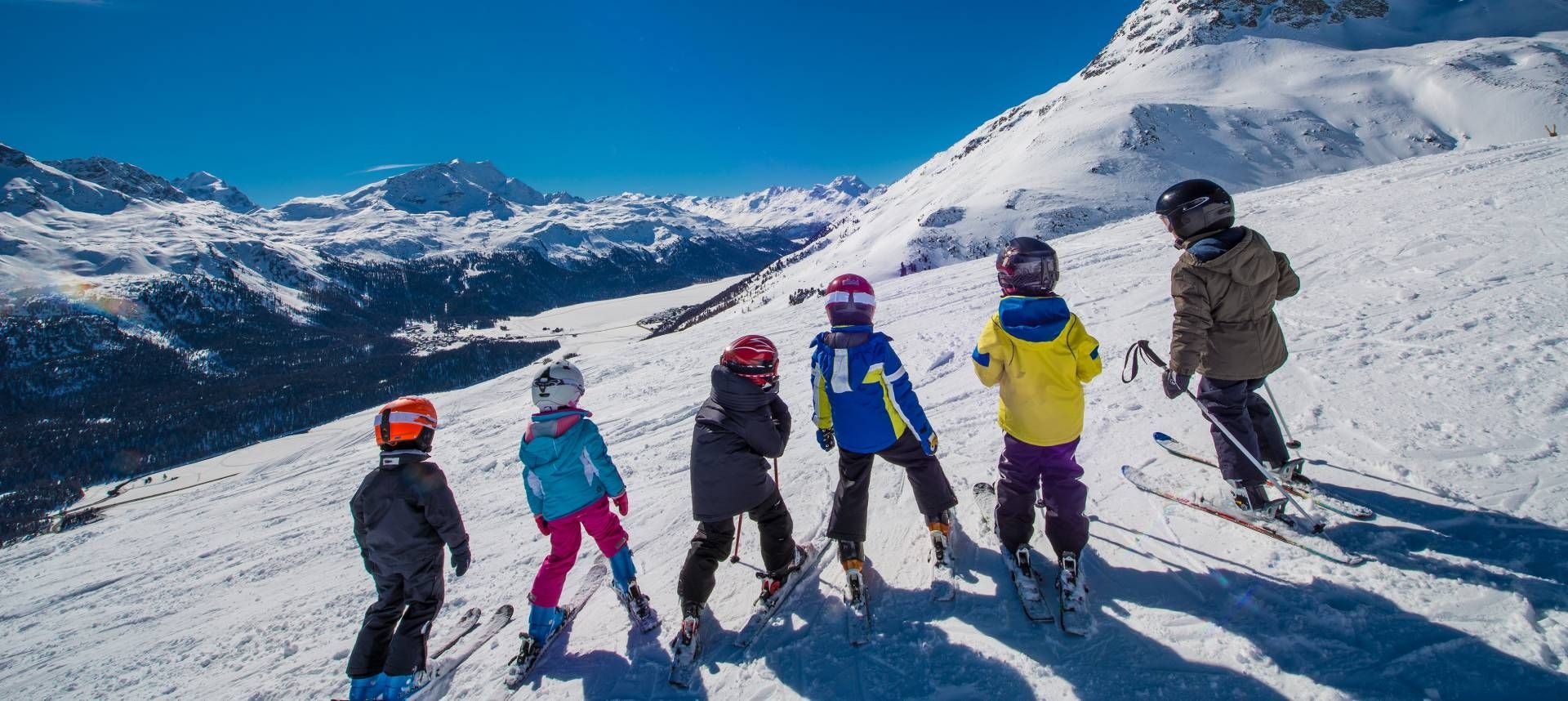 Five skiers standing on a snowy mountain slope under a bright blue sky
