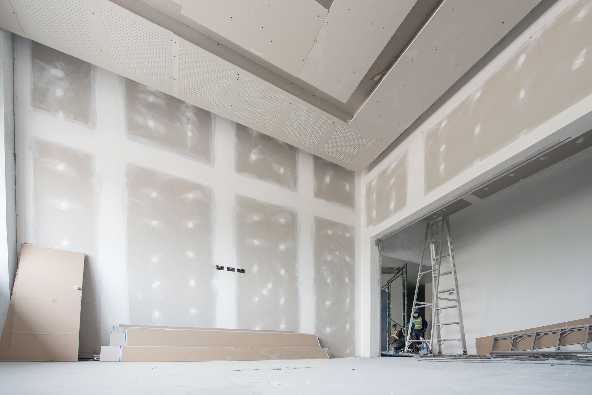 Room under construction, drywall installed on walls and ceiling, ladder present.