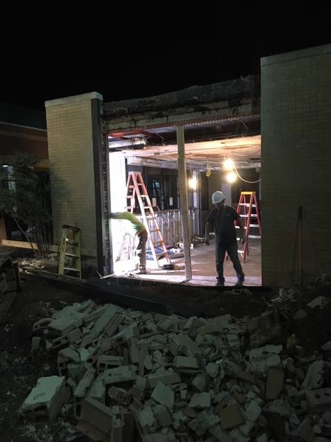Construction site at night. Workers inside a building frame, rubble in the foreground.