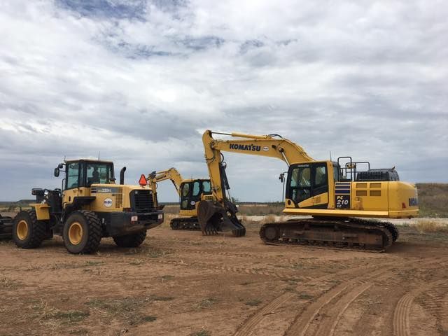 Three yellow construction vehicles on brown dirt under a cloudy sky.