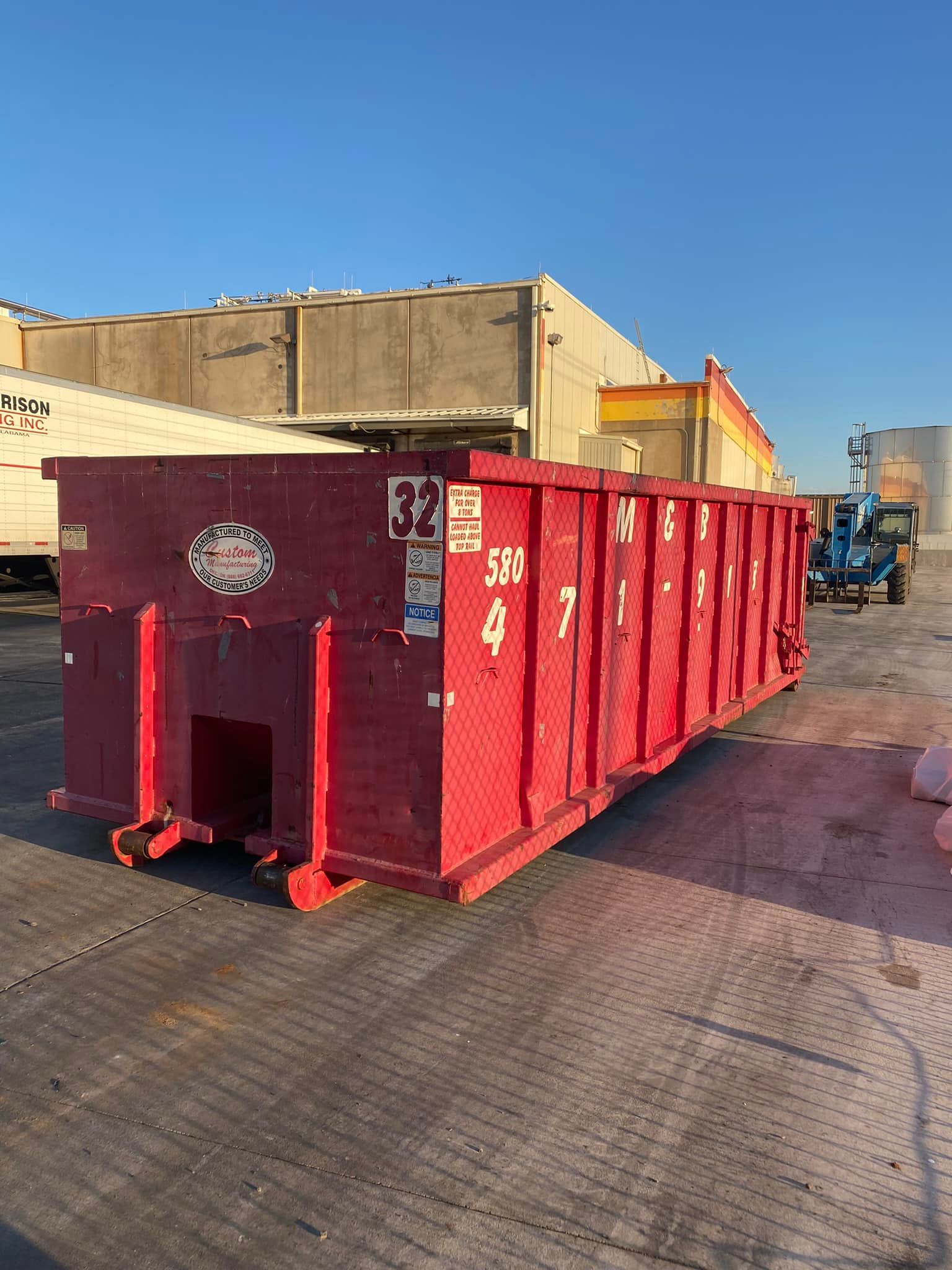 Red dumpster on a concrete surface, numbers visible, with a building and sky in the background.