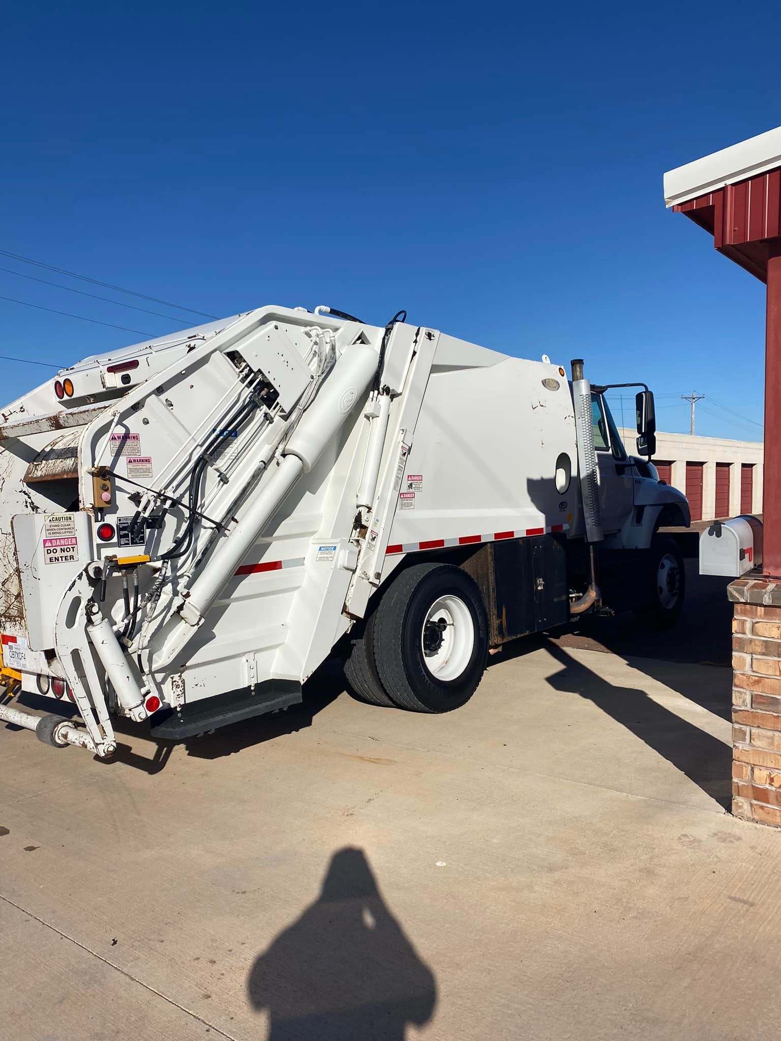 White garbage truck parked next to a building on a sunny day.