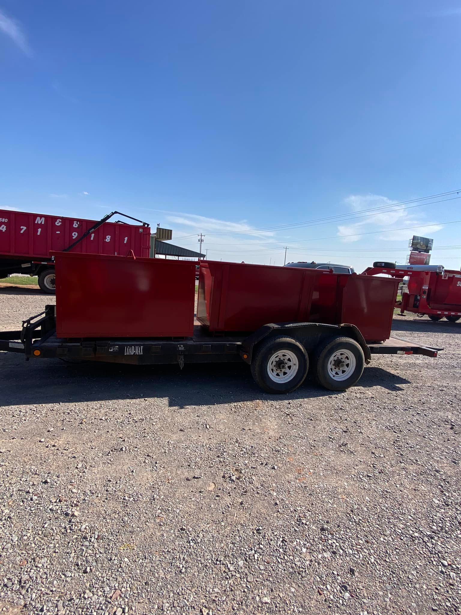 Red dump trailer on a gravel lot under a blue sky, with other red containers in the background.