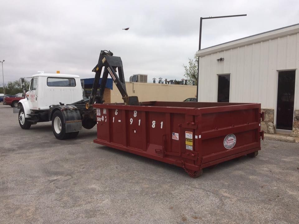 A red dumpster being loaded onto a white truck in a parking lot.