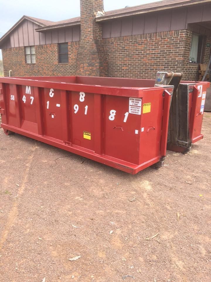 Red rectangular dumpster in front of a brick house.