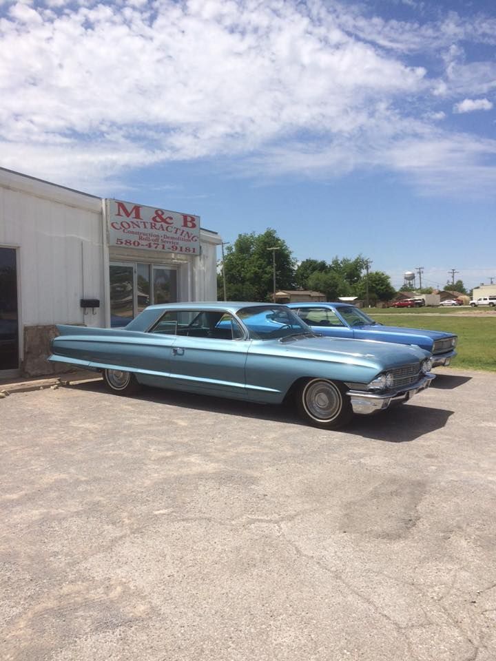Blue vintage car parked in front of M&B Construction building on a sunny day.