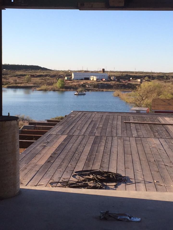 Wooden deck overlooking a lake, with a building in the distance under a blue sky.