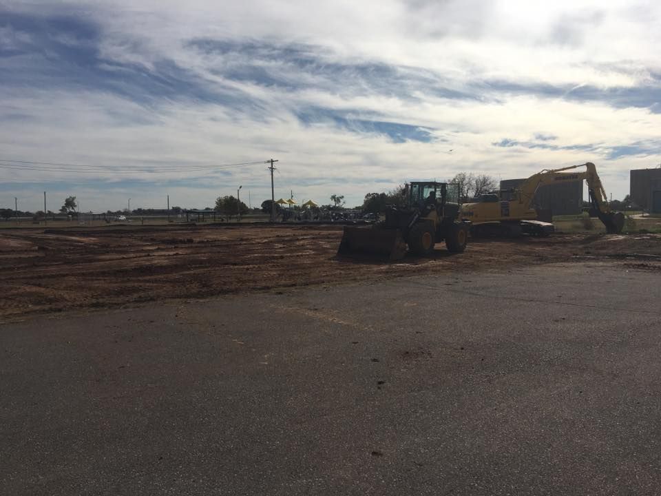 Construction site with heavy machinery, clearing land under a cloudy sky.