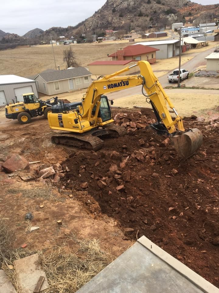Yellow Komatsu excavator digging earth in a construction site, with a town in the background.