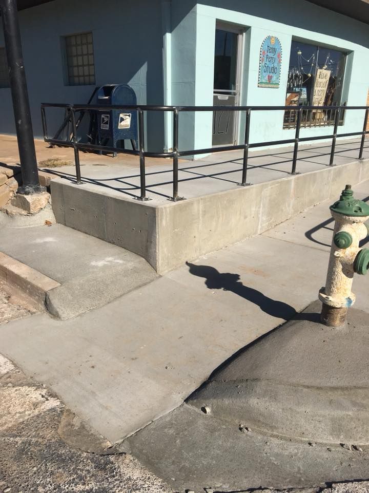 Concrete ramp and steps lead to a light blue building with a black railing, mailbox, and a green fire hydrant.