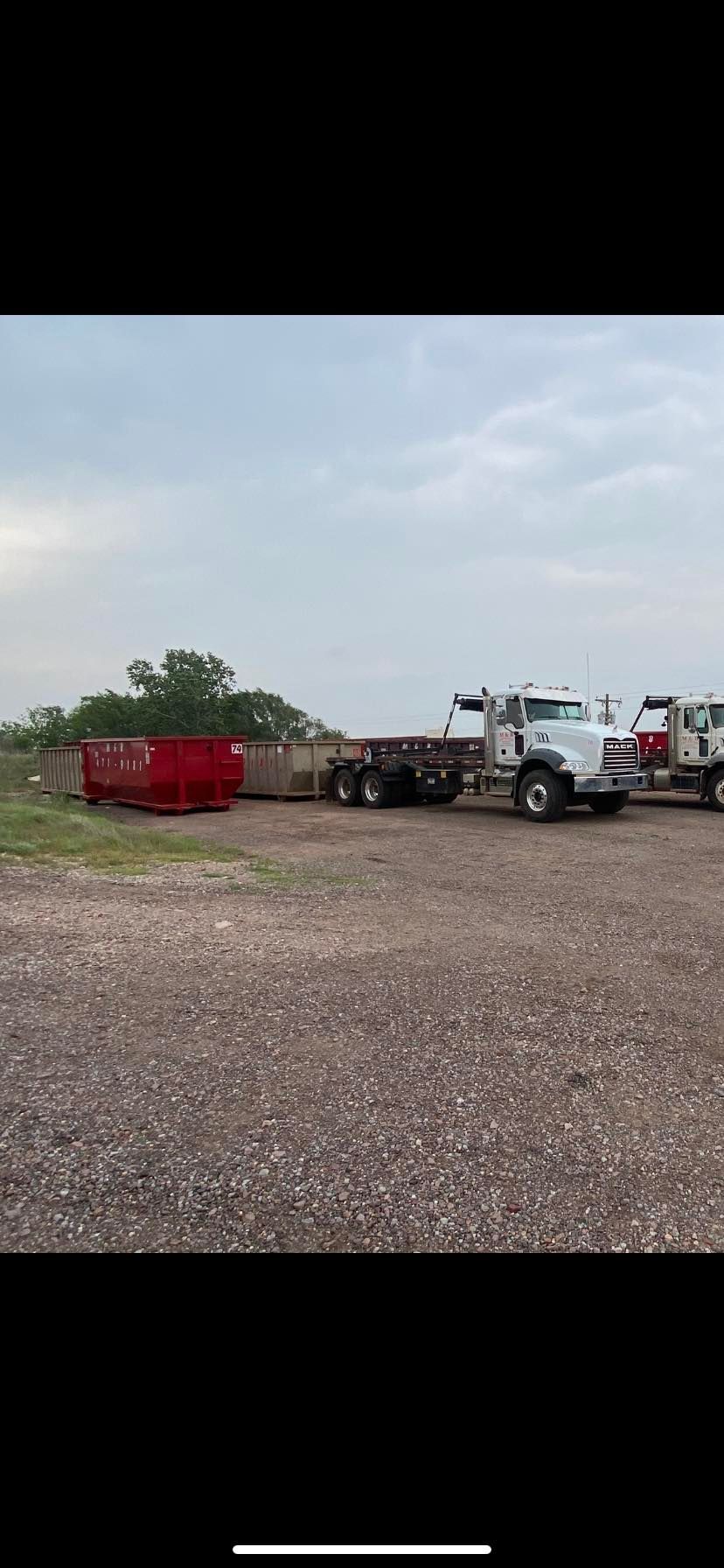 White semi-truck hauling a red container on a gravel lot under a cloudy sky.