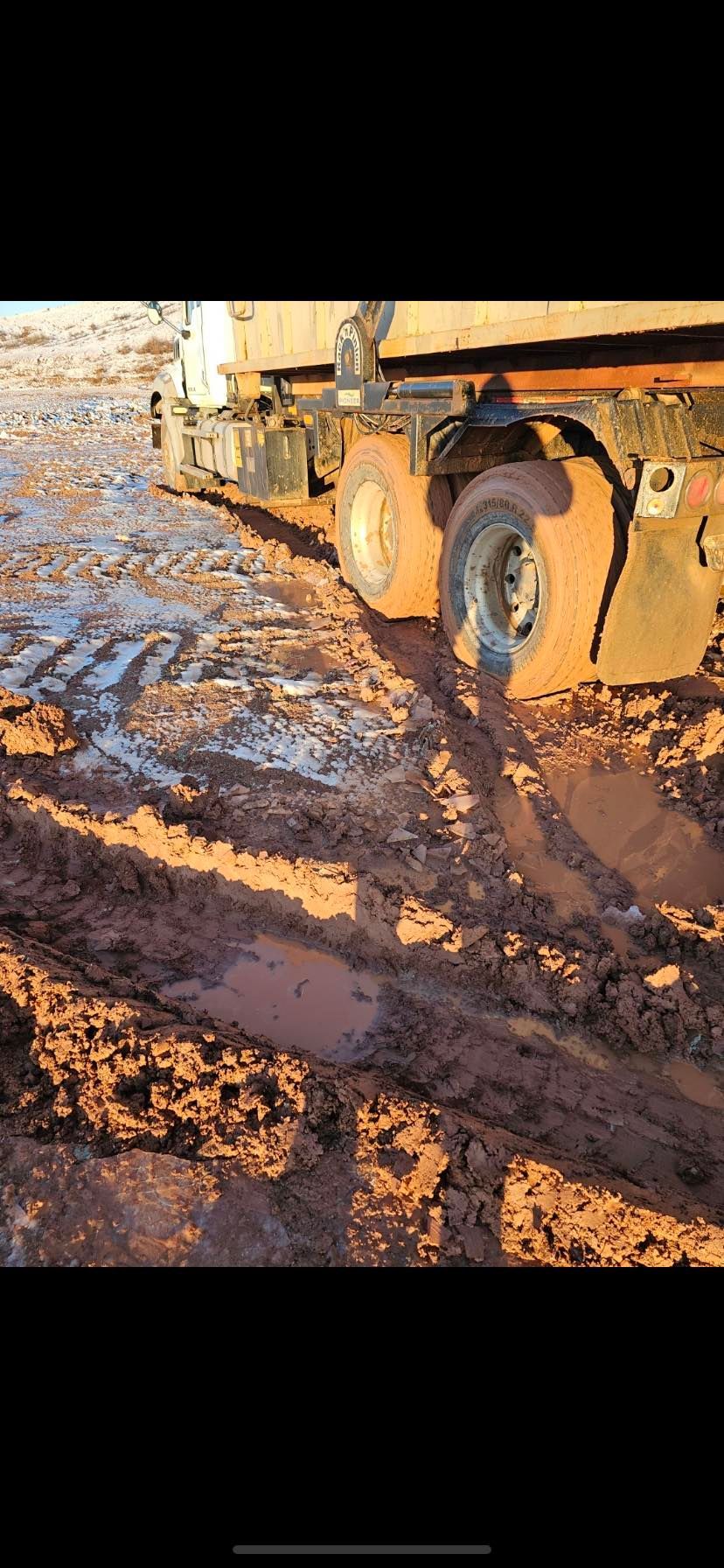 A truck stuck in thick, muddy terrain with tire tracks in reddish-brown soil.