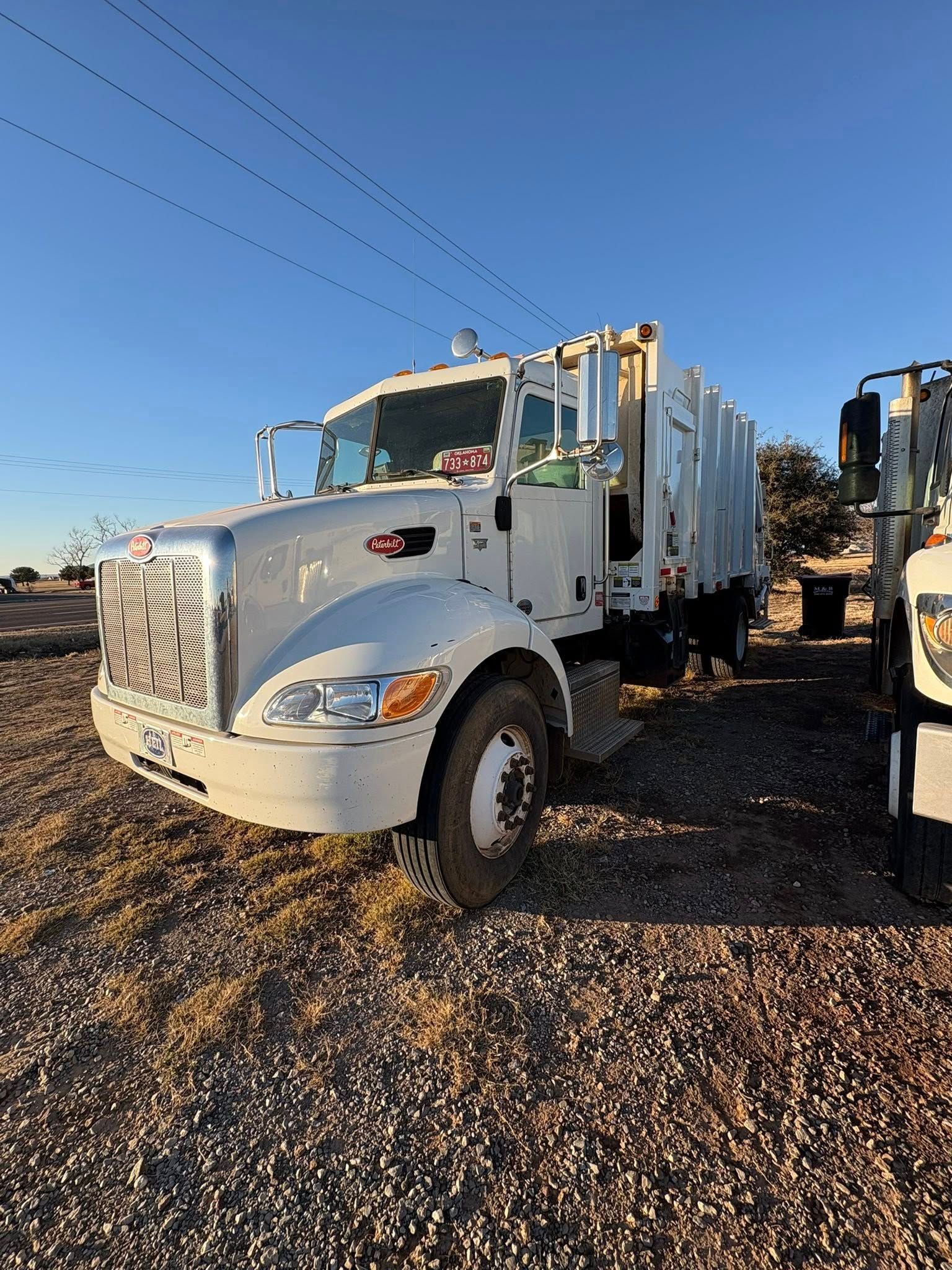 White garbage truck parked outdoors on a sunny day.