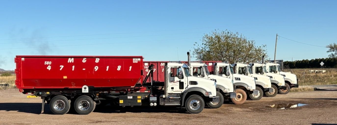 A line of white dump trucks parked on dirt under a blue sky, one with a red container.