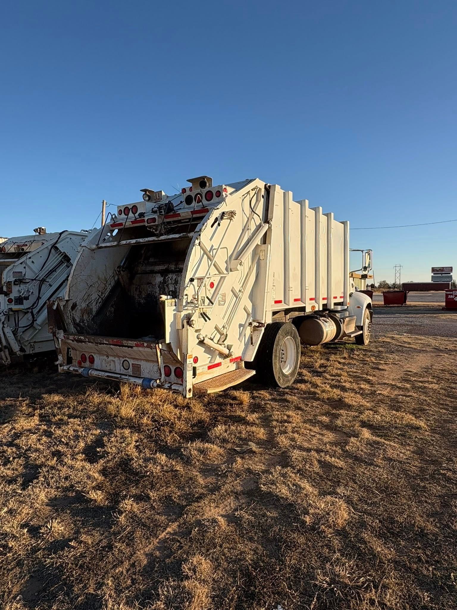 White garbage truck in a field under a clear blue sky.