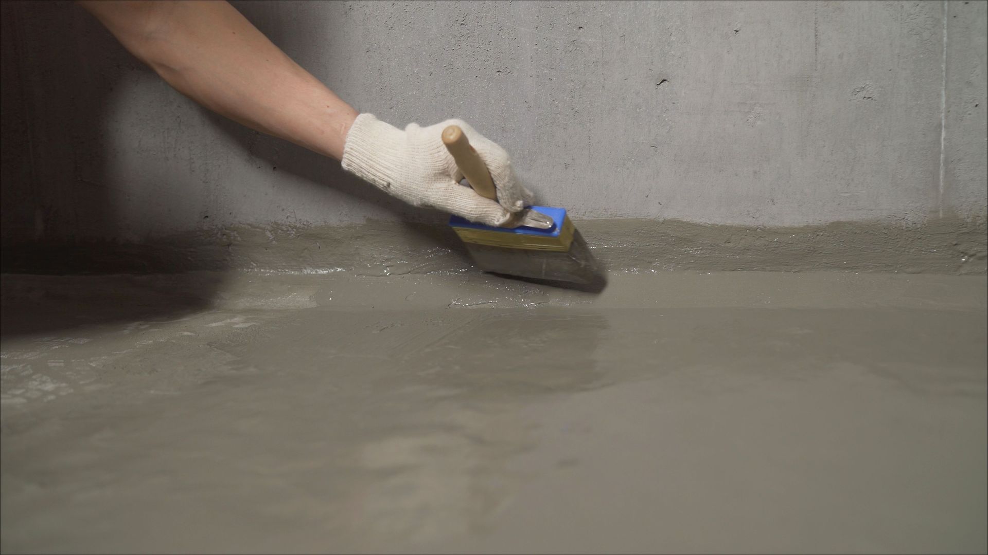 Gloved hand smoothing wet concrete with a trowel along a wall