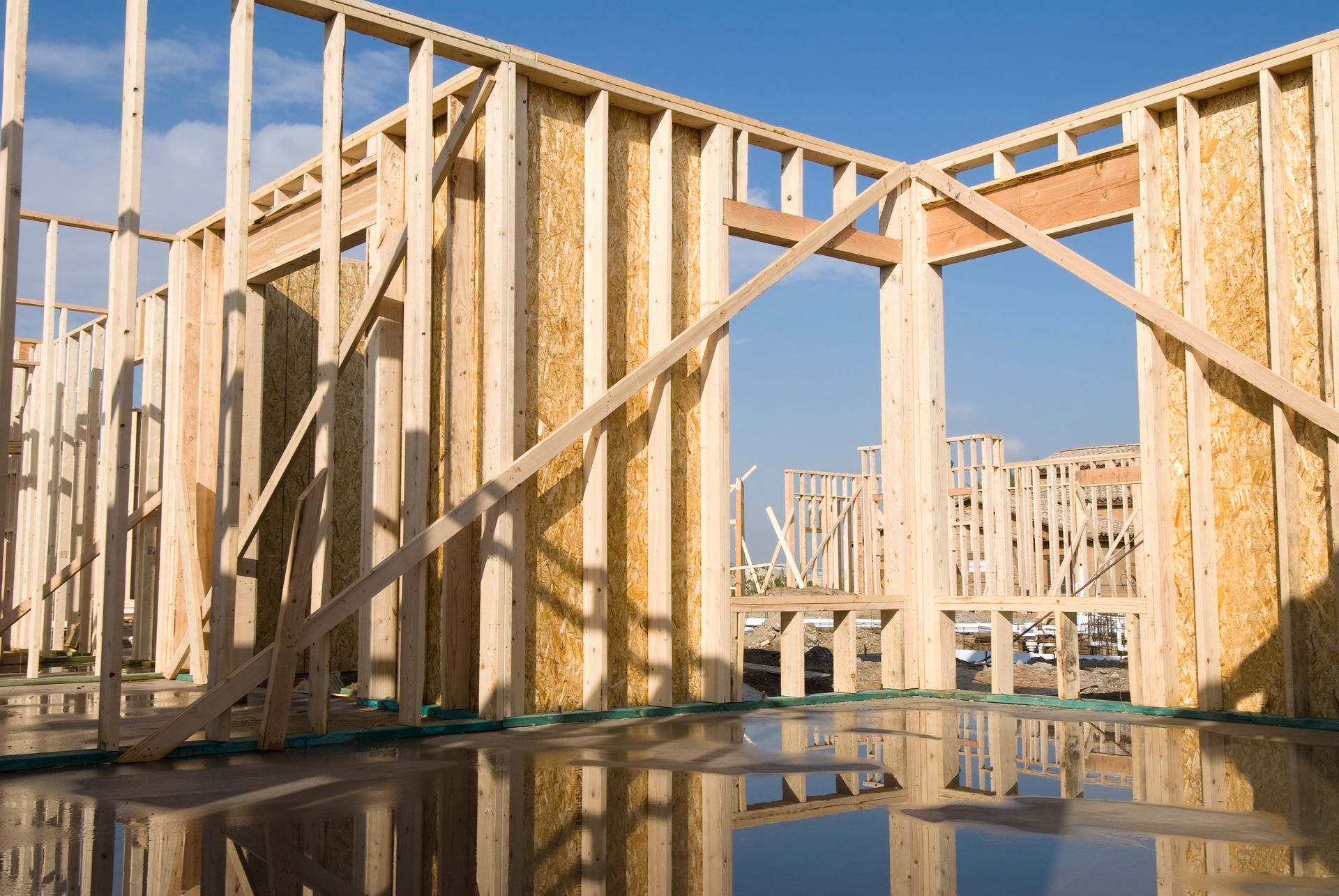 Wood-framed house under construction with plywood walls and reflections in a puddle