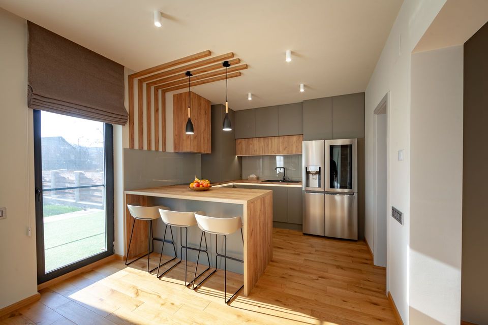Modern kitchen with wood cabinets, island, bar stools, and stainless steel appliances by a window