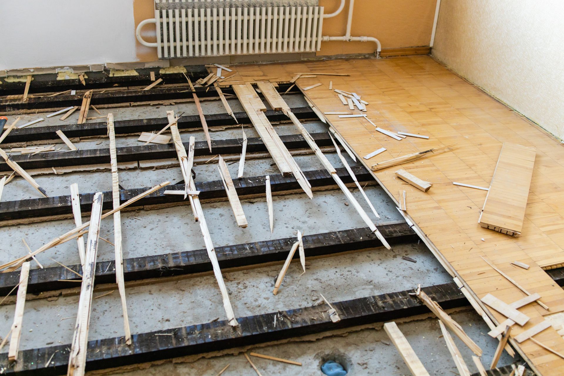 Partially dismantled wooden floor with exposed joists in a room, tools scattered nearby