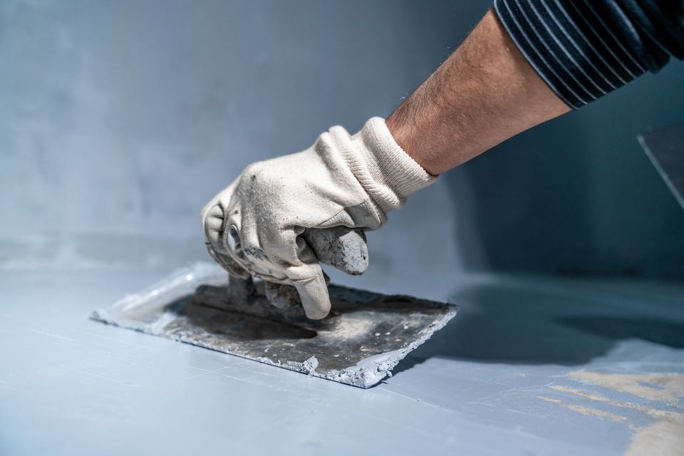 Gloved hand smoothing wet gray sealant on a floor with a trowel