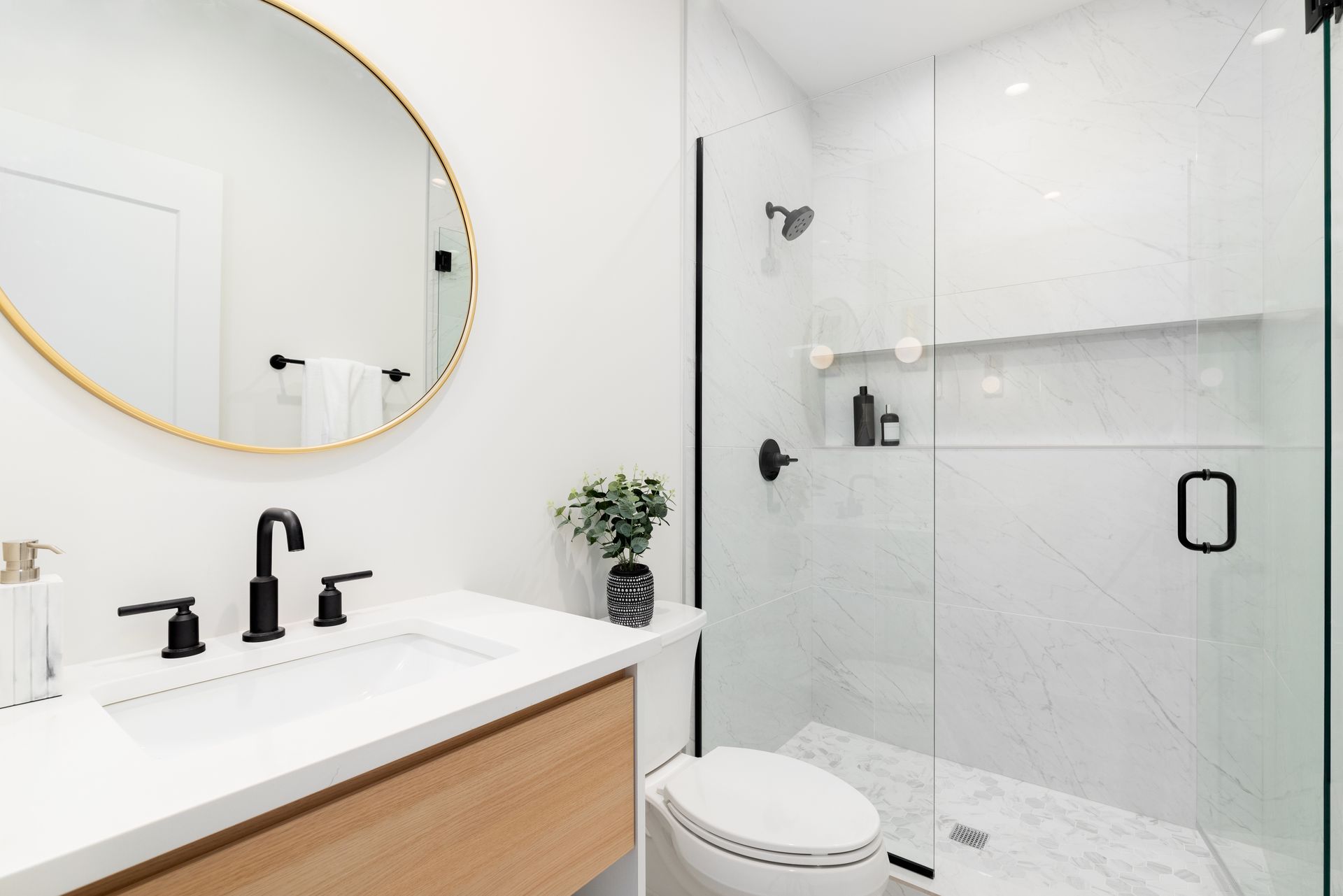 Bright modern bathroom with white shower, round gold mirror, and black fixtures