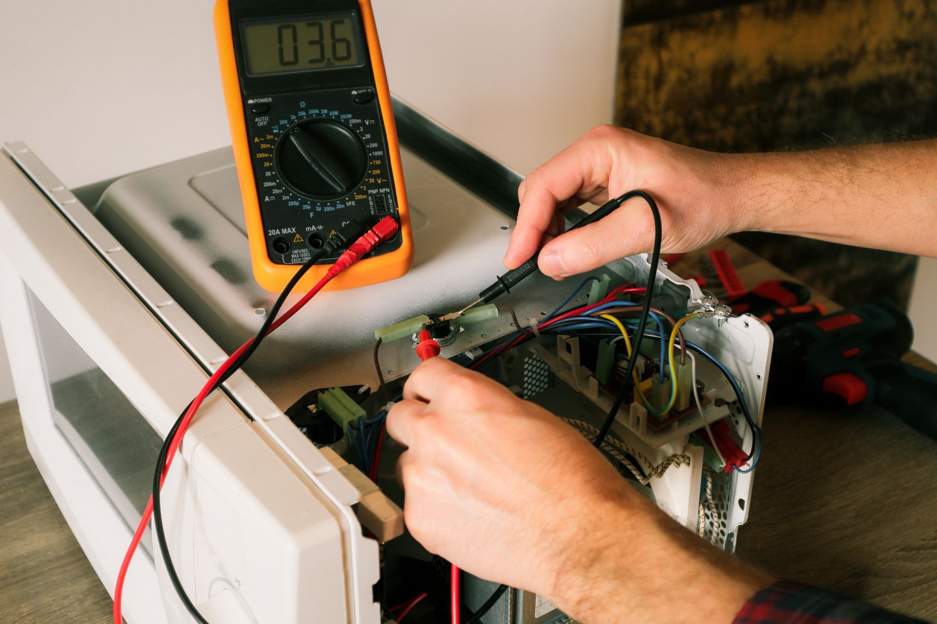 Person using a multimeter to test electronics inside an open device, with wires exposed on a workbench.