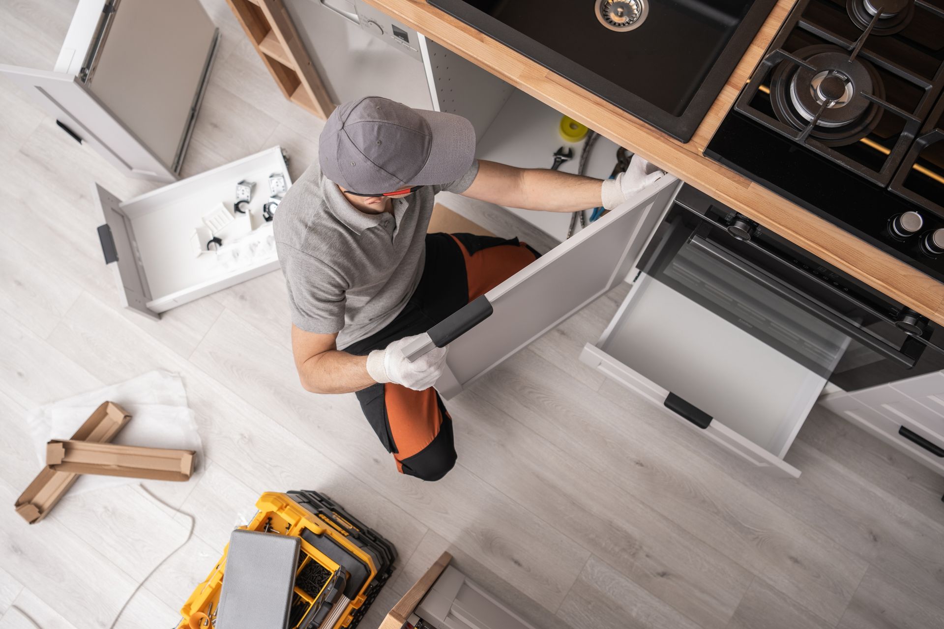 Worker installing kitchen cabinet doors with a cordless drill in a modern kitchen.
