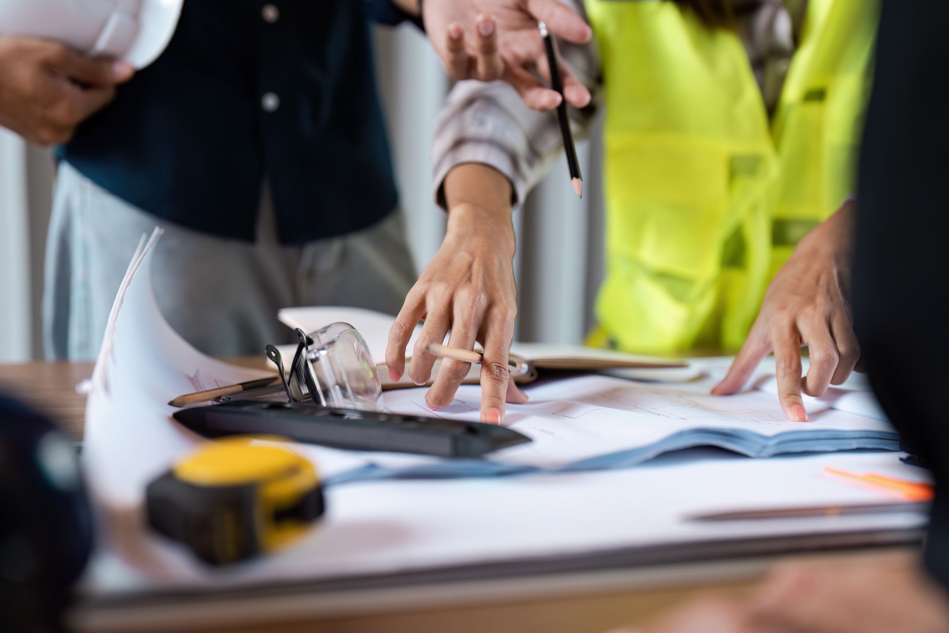People reviewing blueprints on a table at a construction site, with a hard hat and safety vest visible.