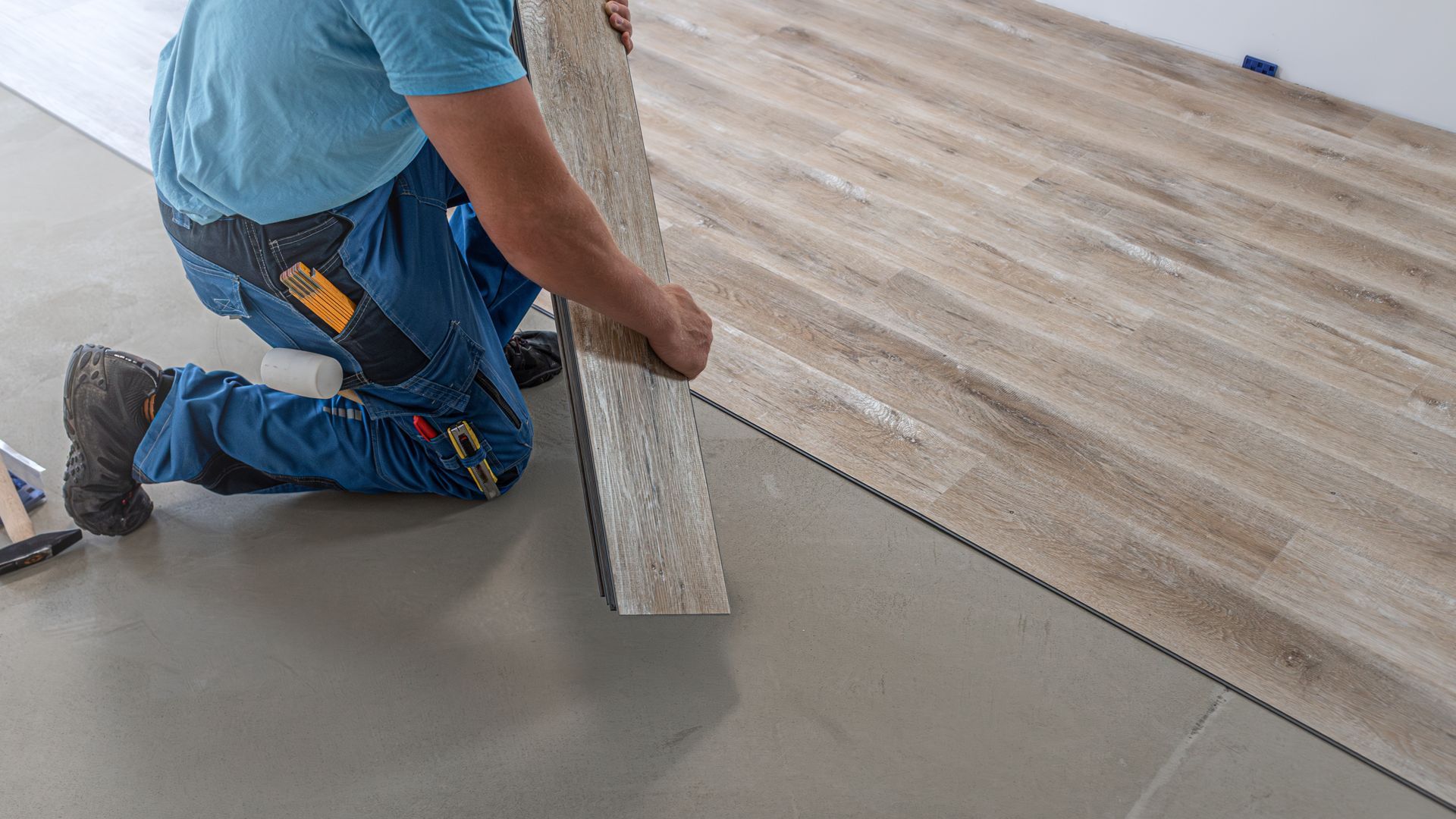 Worker installing wood-look flooring on a gray concrete floor