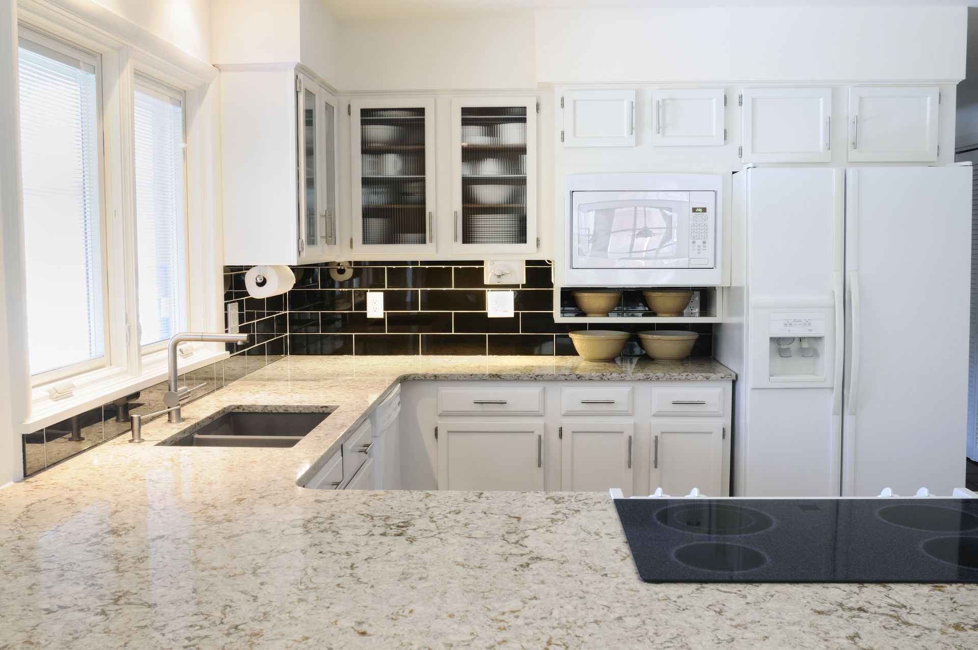 Bright modern kitchen with white cabinets, black tile backsplash, and granite countertops