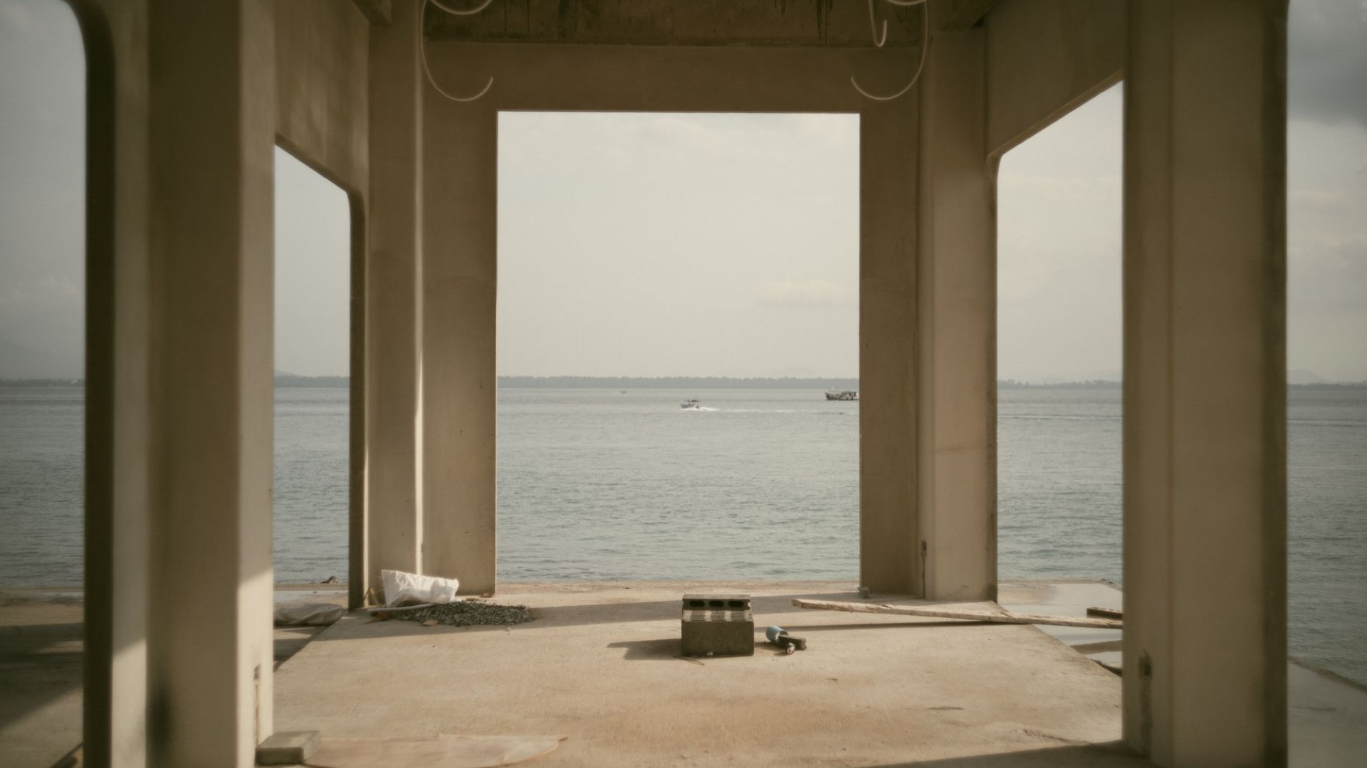 An unfinished concrete structure open to the sea, with building materials left on the floor.
